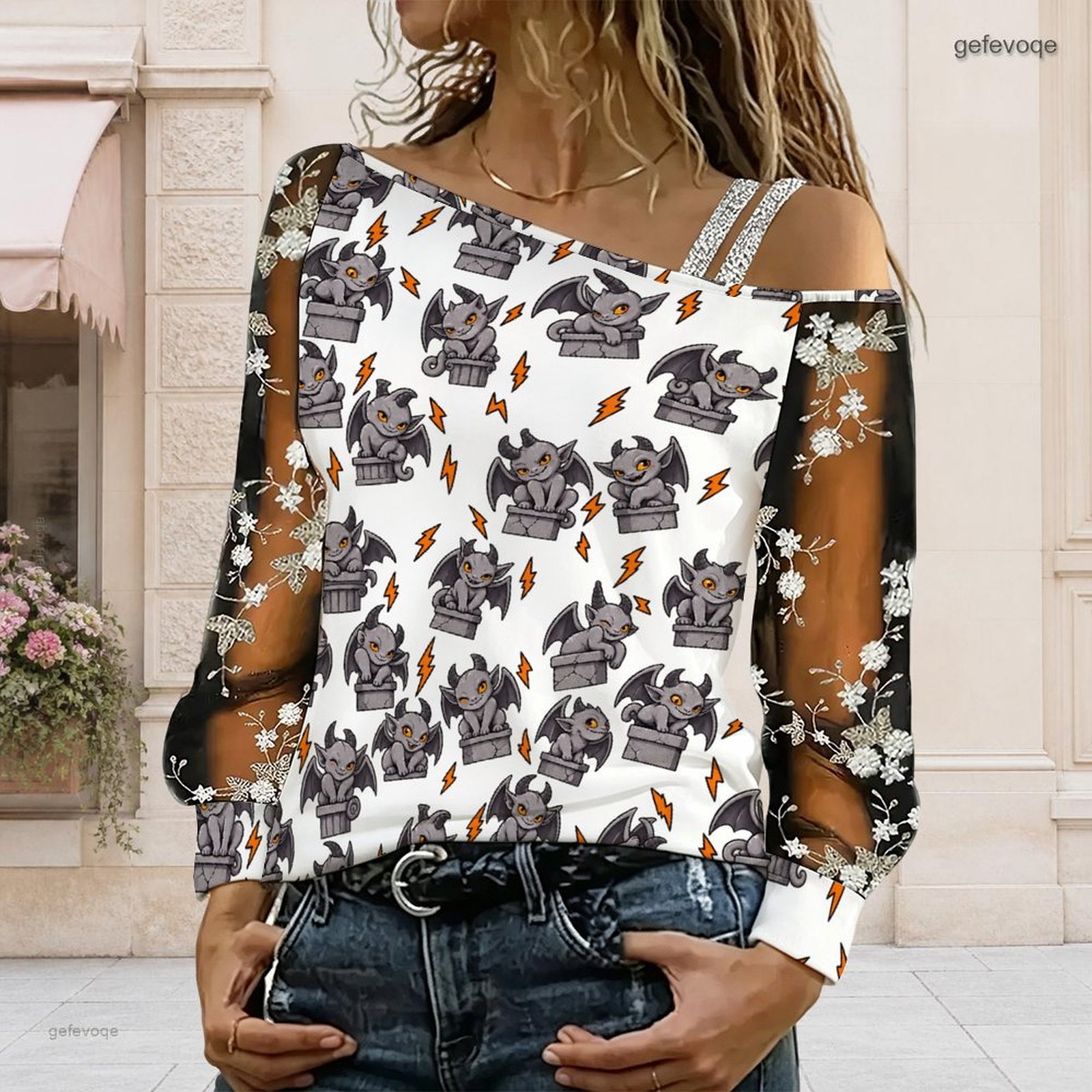 Blouse Off Shoulder - 女性用、アシンメトリーなオフショルダーのトップス。漫画風のガーゴイルと稲妻のプリントが施され、長めのシアー素材のメッシュに花柄の刺繍が施されたブラウス。